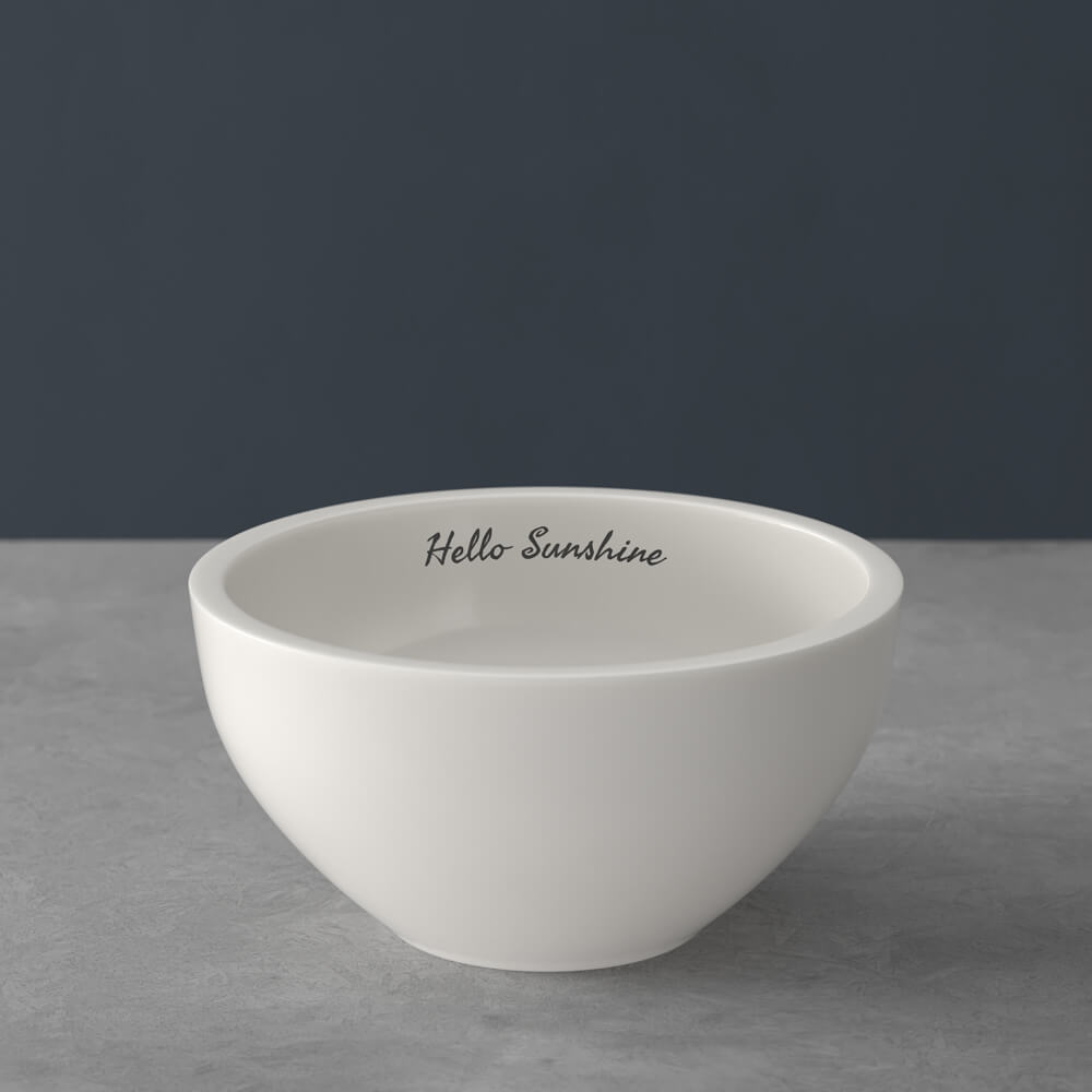 Weiße Keramikschale mit dem Aufdruck "Hello Sunshine" auf dem inneren Rand, auf einer grauen Fläche mit dunklem Hintergrund.