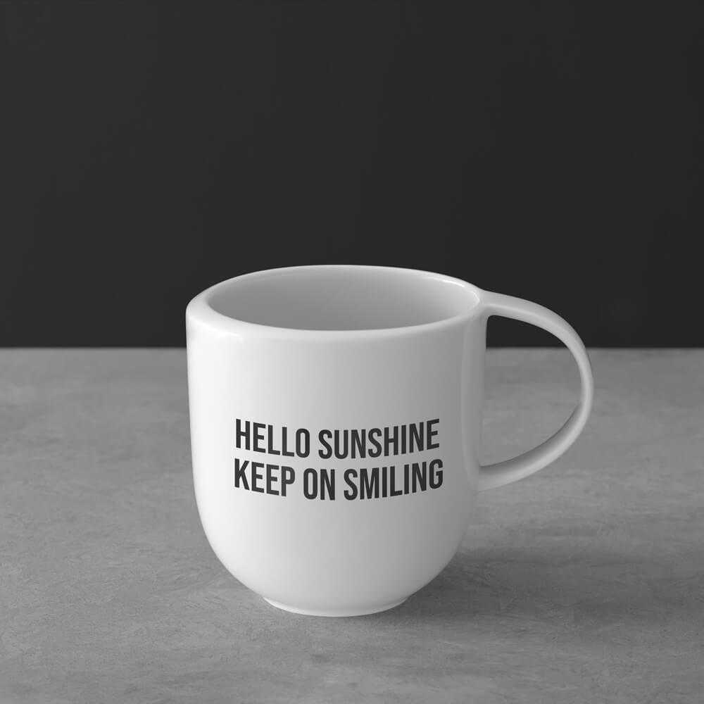 1042649651_Bebas-Neue_schwarz Weißer Becher mit der Aufschrift "HELLO SUNSHINE KEEP ON SMILING" in schwarzer Schrift auf grauer Oberfläche.